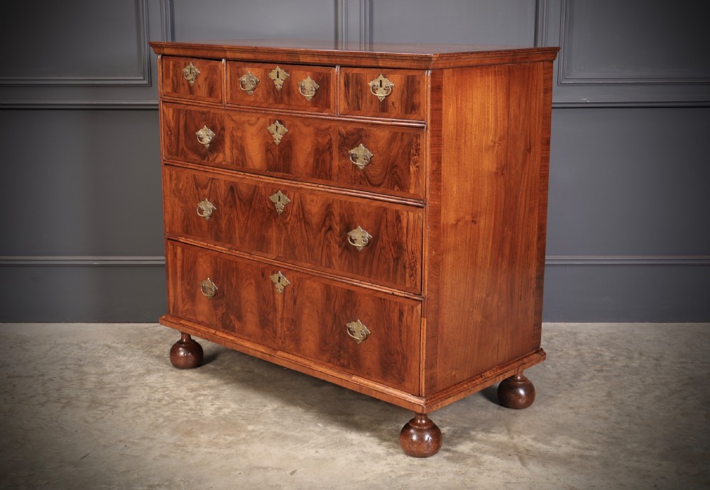 A Queen Anne style warm brown walnut chest of drawers featuring inlaid geometric top decoration, brass drop handles, keyhole escutcheons, and turned bun feet. View VII