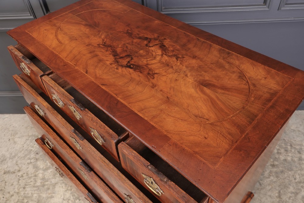 A Queen Anne style warm brown walnut chest of drawers featuring inlaid geometric top decoration, brass drop handles, keyhole escutcheons, and turned bun feet. View X
