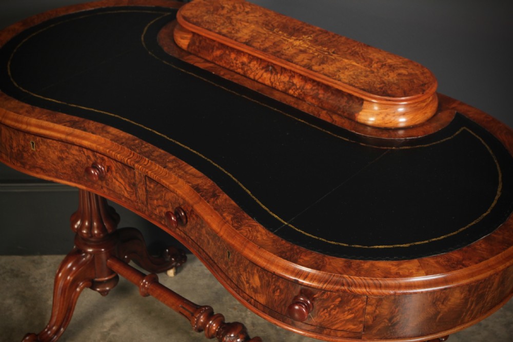 A Victorian burr walnut kidney-shaped writing table featuring a black leather insert, inlaid marquetry, raised caddy, frieze drawers, and carved legs on castors. View VI