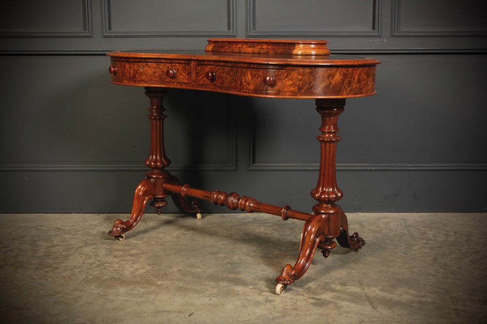A Victorian burr walnut kidney-shaped writing table featuring a black leather insert, inlaid marquetry, raised caddy, frieze drawers, and carved legs on castors. View X