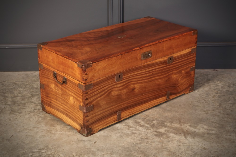 An antique camphor wood military campaign trunk with protective brass corner straps, flush brass fittings, and side carrying handles.