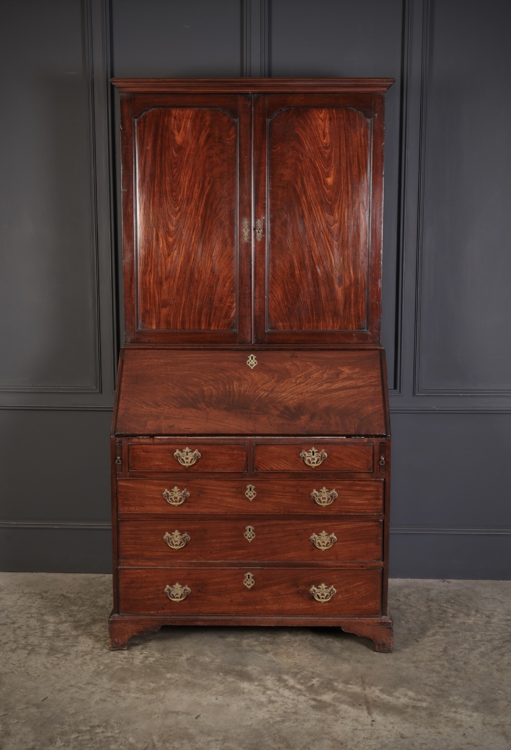 A Georgian rich mahogany bureau bookcase featuring a two-door upper cabinet, slant-front writing bureau, four drawers with brass handles, and bracket feet.