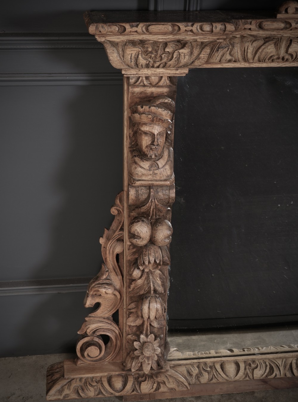 A large Victorian carved oak overmantel mirror featuring detailed carvings of mask heads, fruit garlands, and scrollwork around a rectangular glass plate. View II