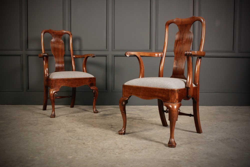A pair of polished mahogany Queen Anne armchairs featuring vasiform back splats, outcurved armrests, cabriole front legs with pad feet, and light neutral upholstered seats.