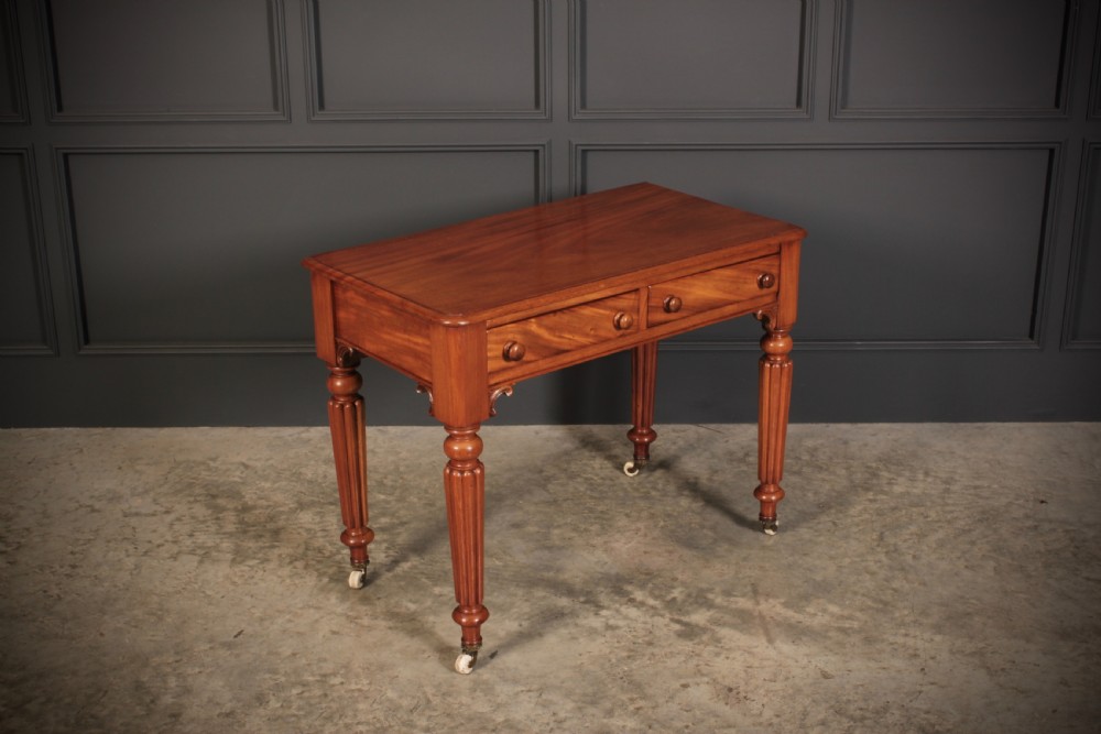 A Victorian mahogany side table featuring two front drawers with wooden turned knobs and four reeded legs resting on ceramic castors. View II