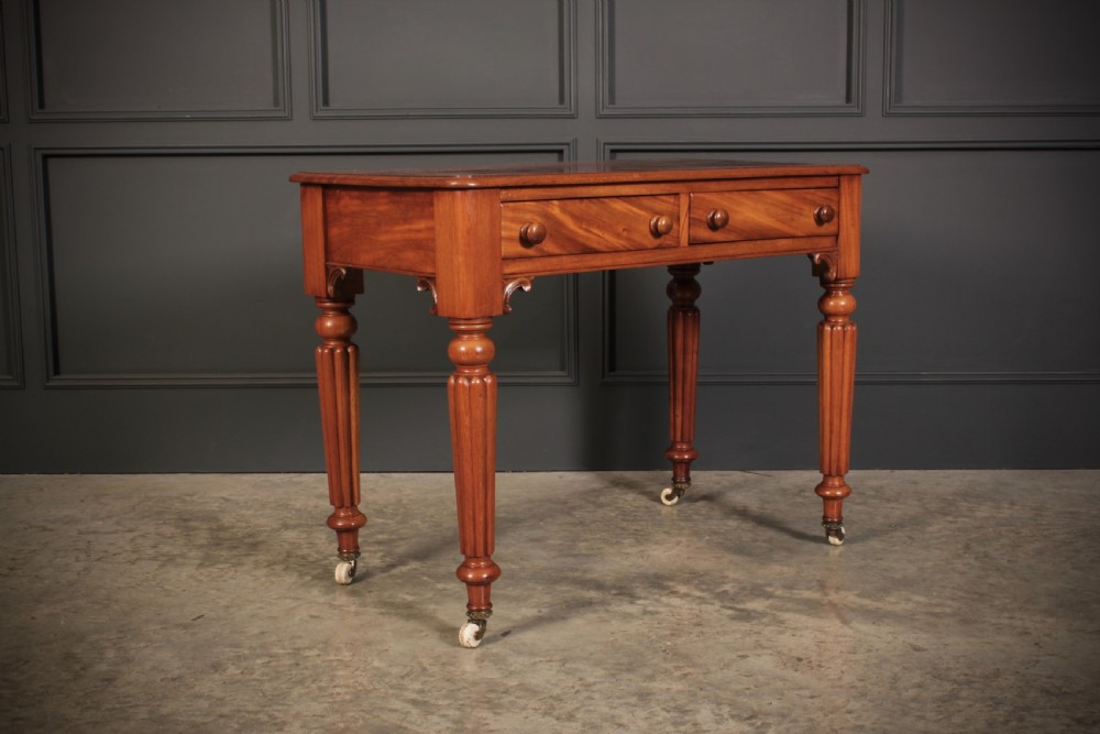 A Victorian mahogany side table featuring two front drawers with wooden turned knobs and four reeded legs resting on ceramic castors.