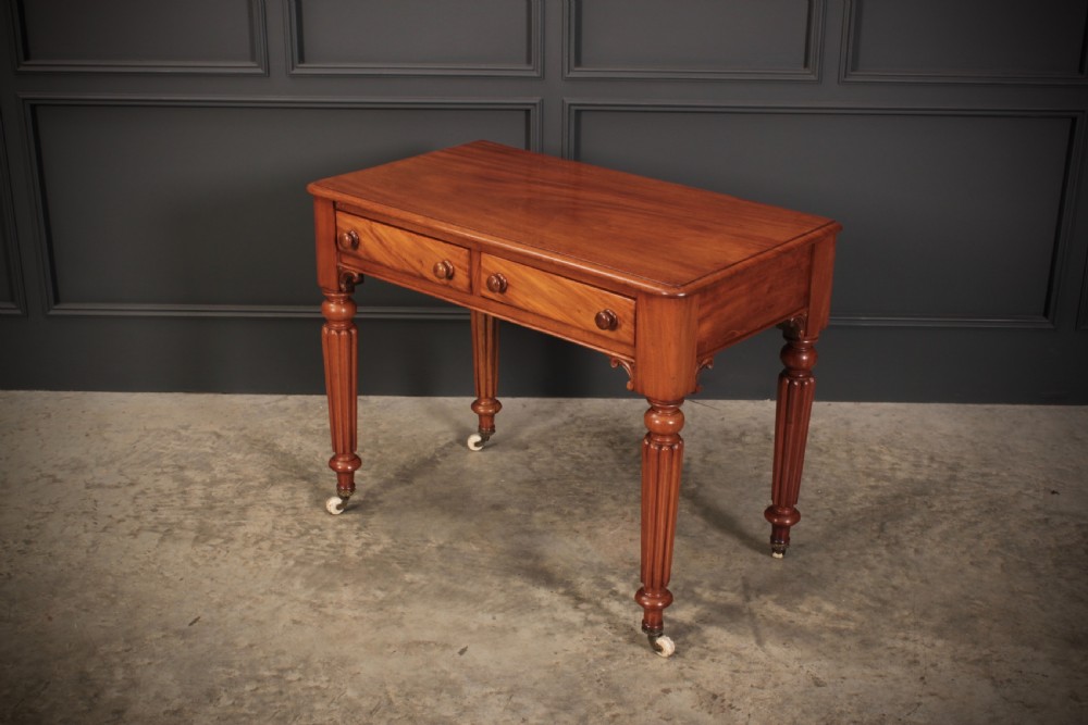 A Victorian mahogany side table featuring two front drawers with wooden turned knobs and four reeded legs resting on ceramic castors. View VI