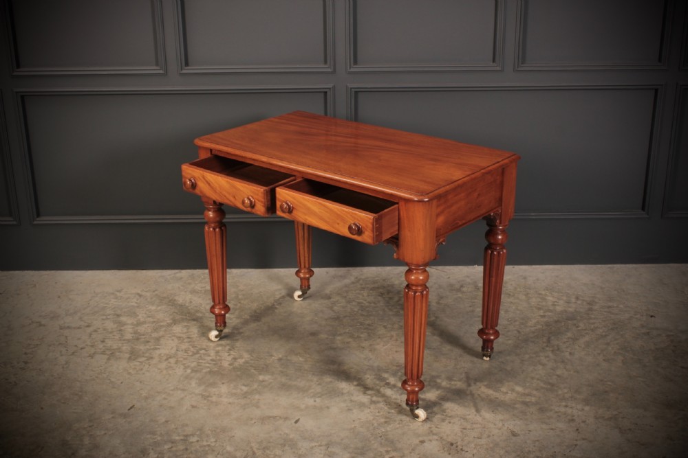 A Victorian mahogany side table featuring two front drawers with wooden turned knobs and four reeded legs resting on ceramic castors. View IX