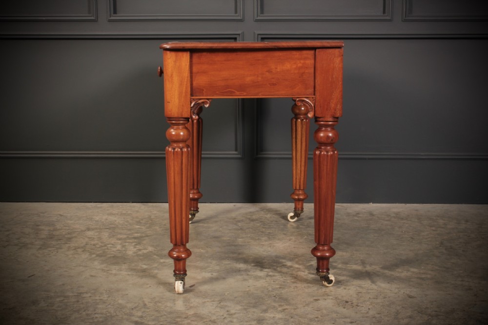 A Victorian mahogany side table featuring two front drawers with wooden turned knobs and four reeded legs resting on ceramic castors. View X