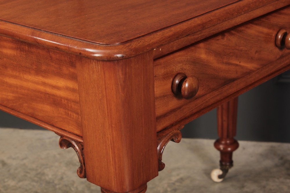 A Victorian mahogany side table featuring two front drawers with wooden turned knobs and four reeded legs resting on ceramic castors. View XII
