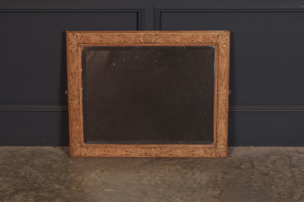 A rectangular wall mirror featuring a carved oak frame with relief acanthus leaf motifs surrounding a central reflective glass panel.