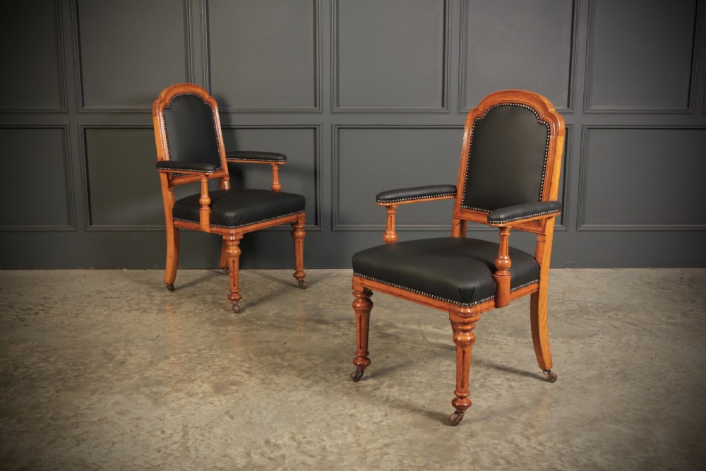 A pair of Victorian oak desk armchairs upholstered in black leather with brass stud trimming and turned legs on castors.