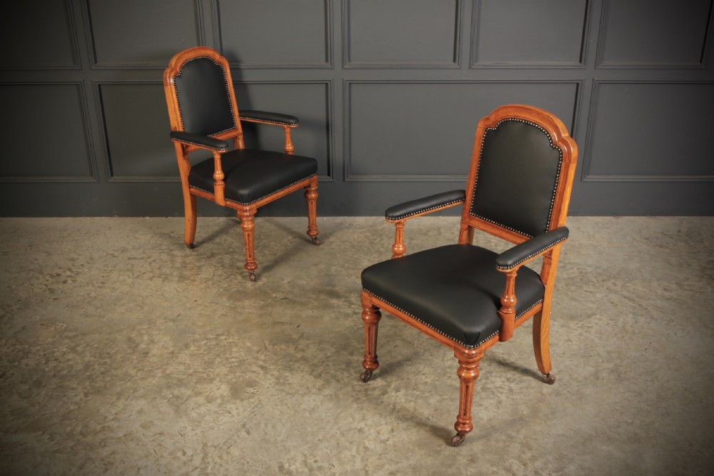 A pair of Victorian oak desk armchairs upholstered in black leather with brass stud trimming and turned legs on castors. View II