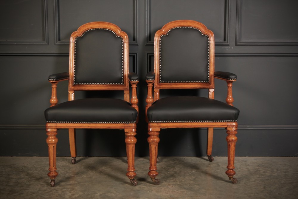 A pair of Victorian oak desk armchairs upholstered in black leather with brass stud trimming and turned legs on castors. View VIII