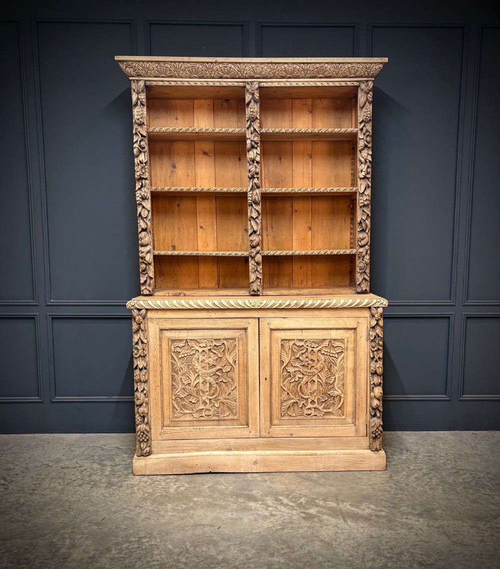 A large two-tier bleached oak open bookcase featuring heavily carved floral pilasters, open adjustable shelves, and a lower cabinet with relief-carved doors. View II