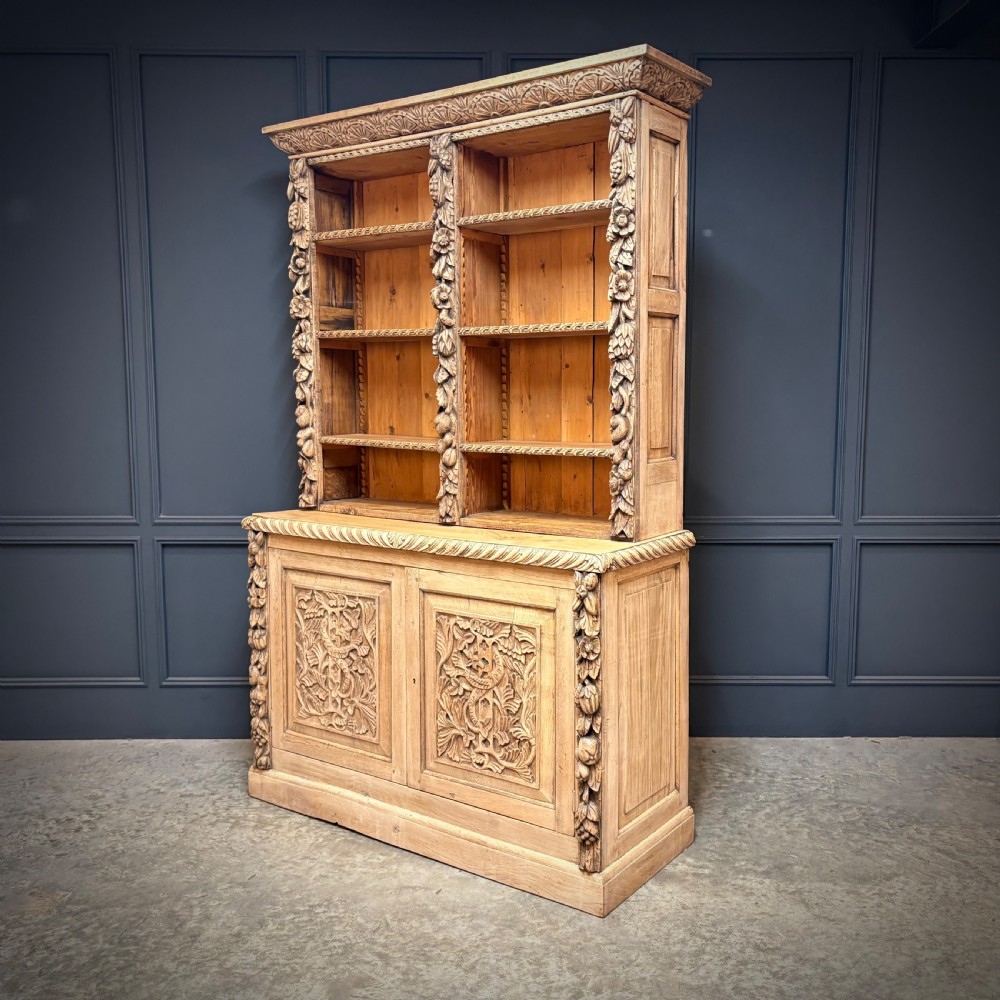 A large two-tier bleached oak open bookcase featuring heavily carved floral pilasters, open adjustable shelves, and a lower cabinet with relief-carved doors. View III