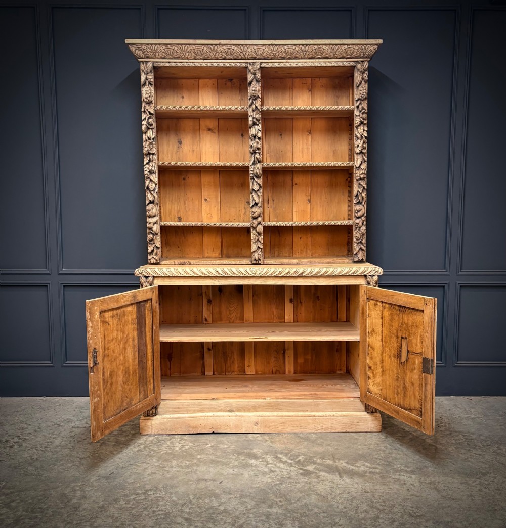 A large two-tier bleached oak open bookcase featuring heavily carved floral pilasters, open adjustable shelves, and a lower cabinet with relief-carved doors. View V