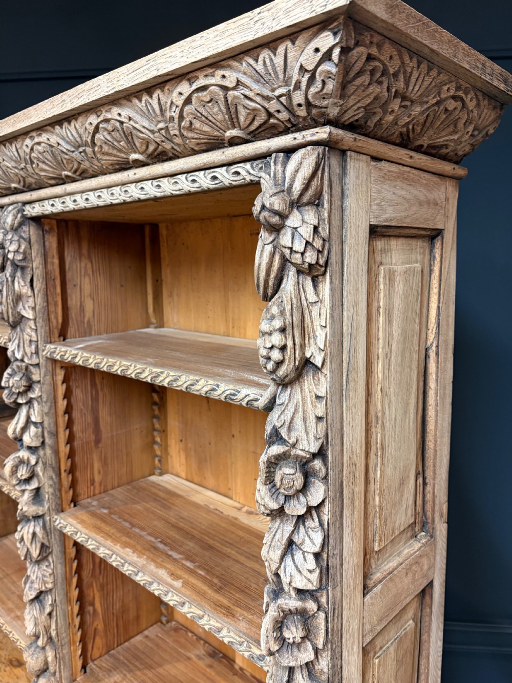A large two-tier bleached oak open bookcase featuring heavily carved floral pilasters, open adjustable shelves, and a lower cabinet with relief-carved doors. View VII