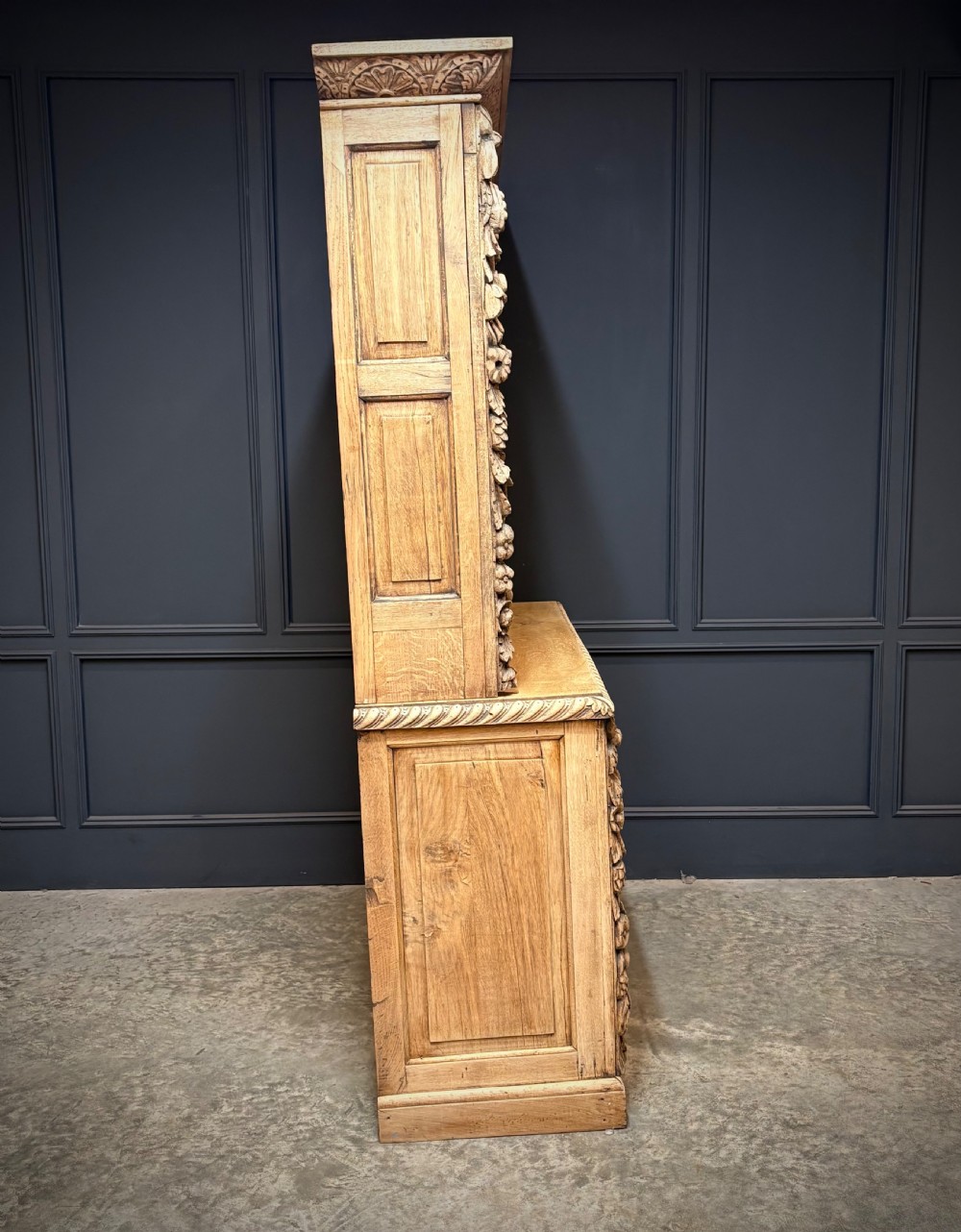 A large two-tier bleached oak open bookcase featuring heavily carved floral pilasters, open adjustable shelves, and a lower cabinet with relief-carved doors. View X