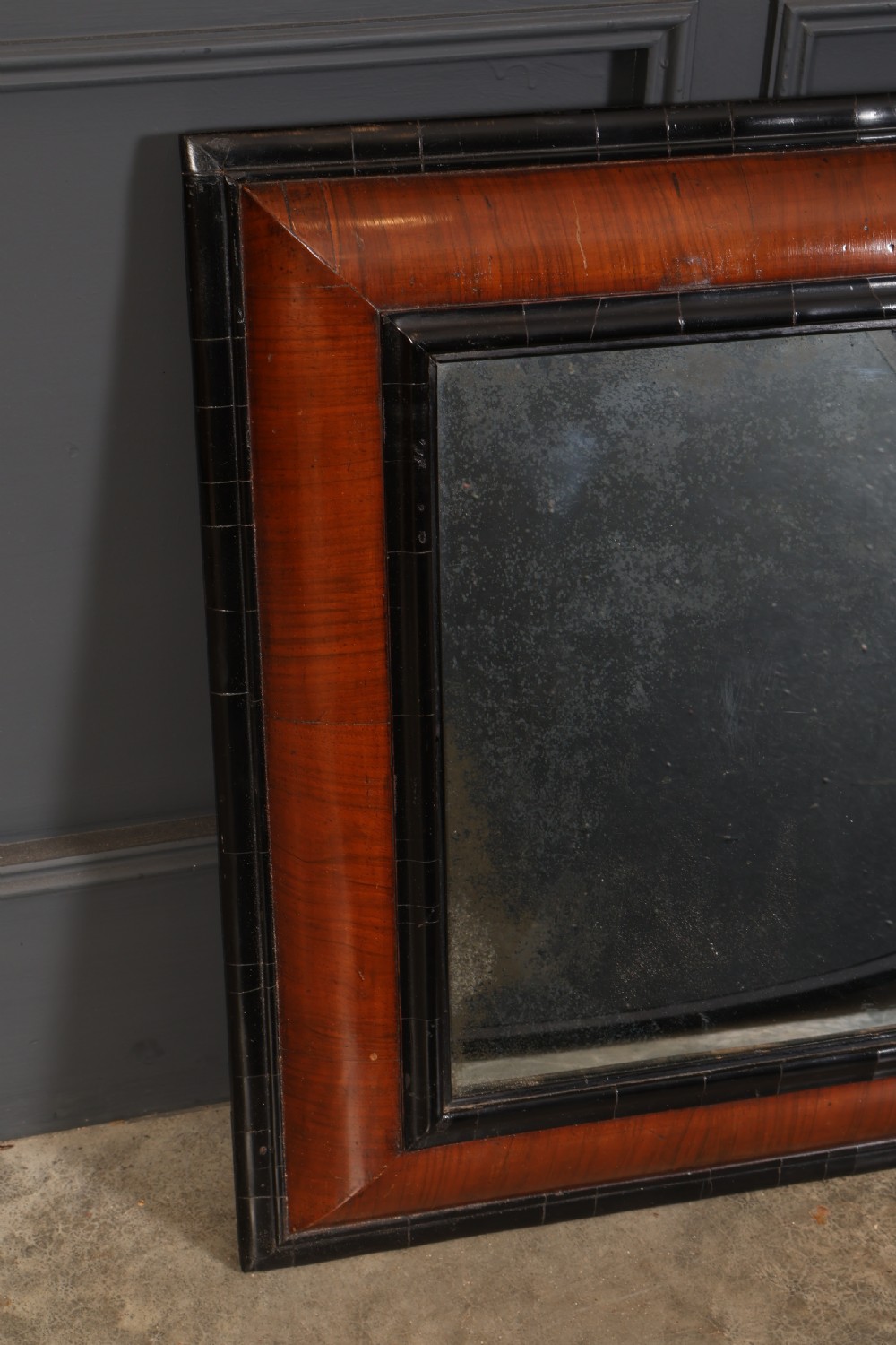 A rectangular antique cushion frame mirror featuring a warm walnut veneer section enclosed by dark ebonised mouldings around an aged glass plate. View IV