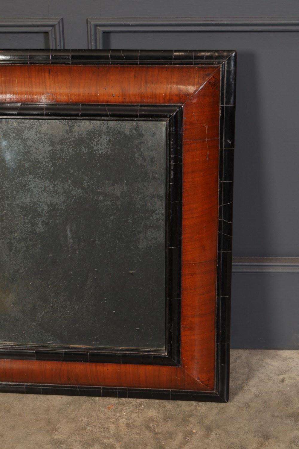 A rectangular antique cushion frame mirror featuring a warm walnut veneer section enclosed by dark ebonised mouldings around an aged glass plate. View III