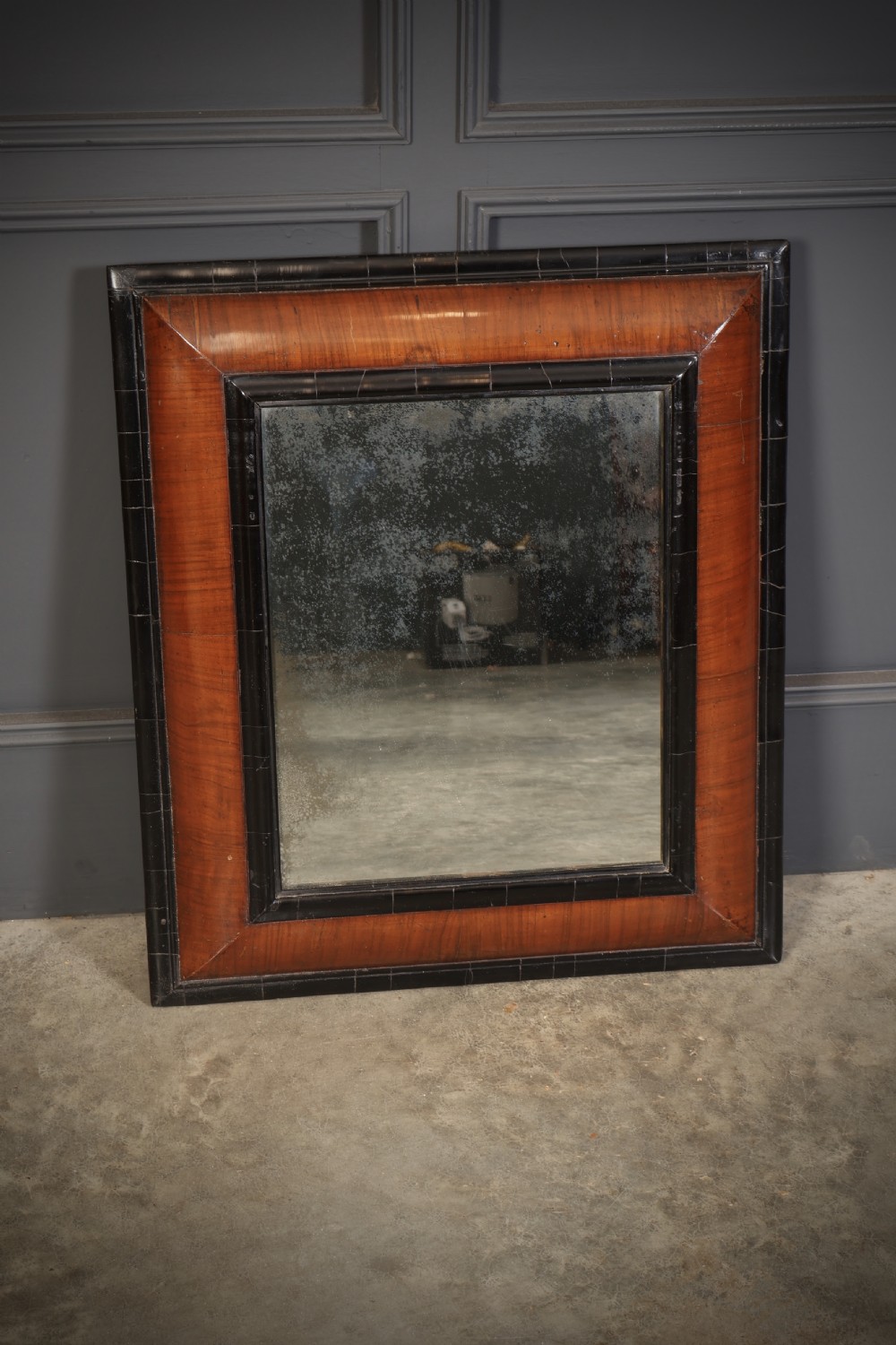A rectangular antique cushion frame mirror featuring a warm walnut veneer section enclosed by dark ebonised mouldings around an aged glass plate. View V