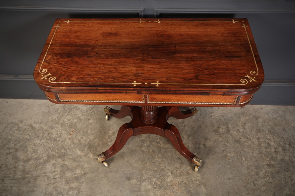 An antique Regency rosewood fold-over card table featuring brass inlay details, a turned pedestal stem, and four swept legs with brass castors. View VIII