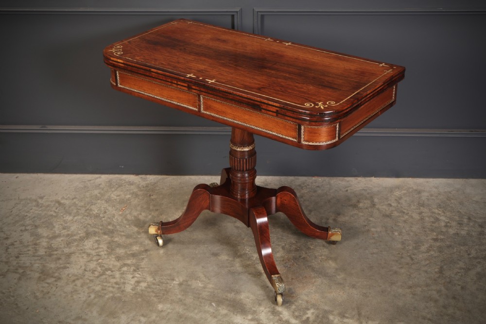 An antique Regency rosewood fold-over card table featuring brass inlay details, a turned pedestal stem, and four swept legs with brass castors. View IX