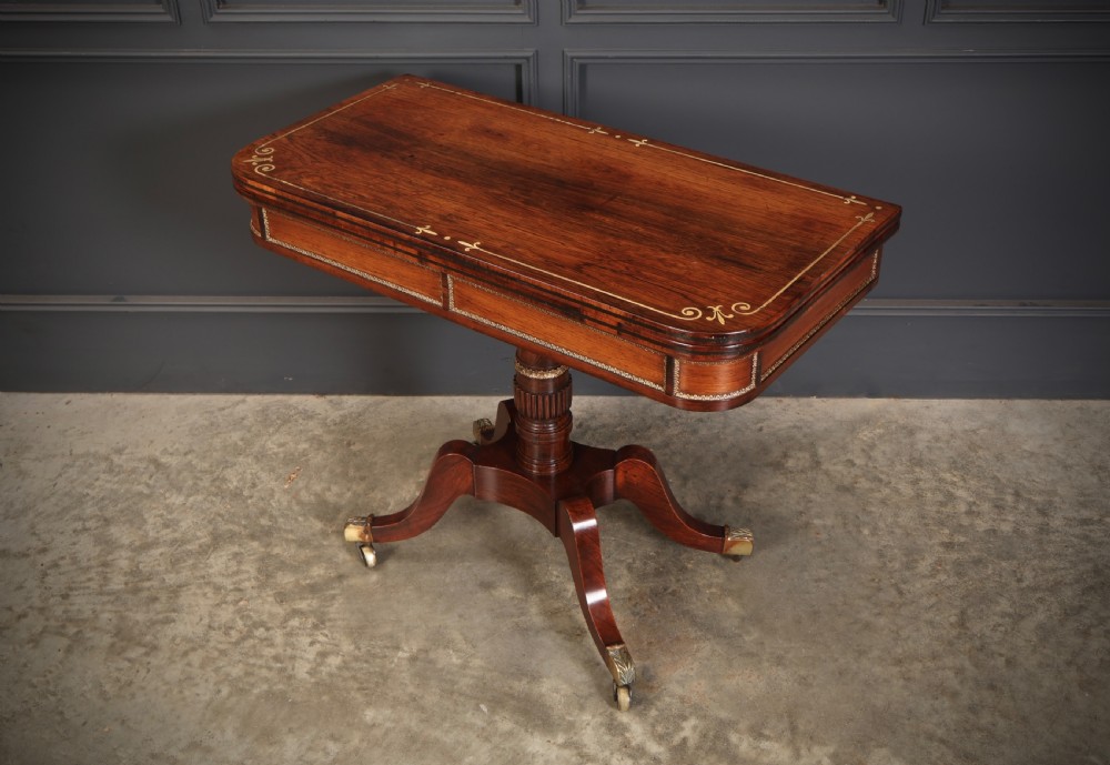 An antique Regency rosewood fold-over card table featuring brass inlay details, a turned pedestal stem, and four swept legs with brass castors. View XI