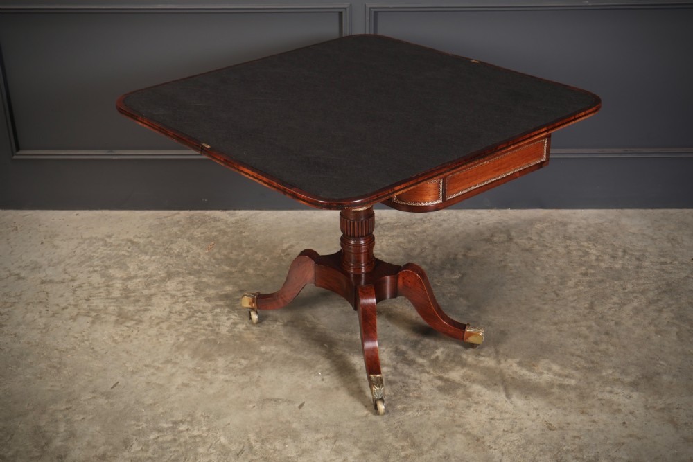 An antique Regency rosewood fold-over card table featuring brass inlay details, a turned pedestal stem, and four swept legs with brass castors. View XIII