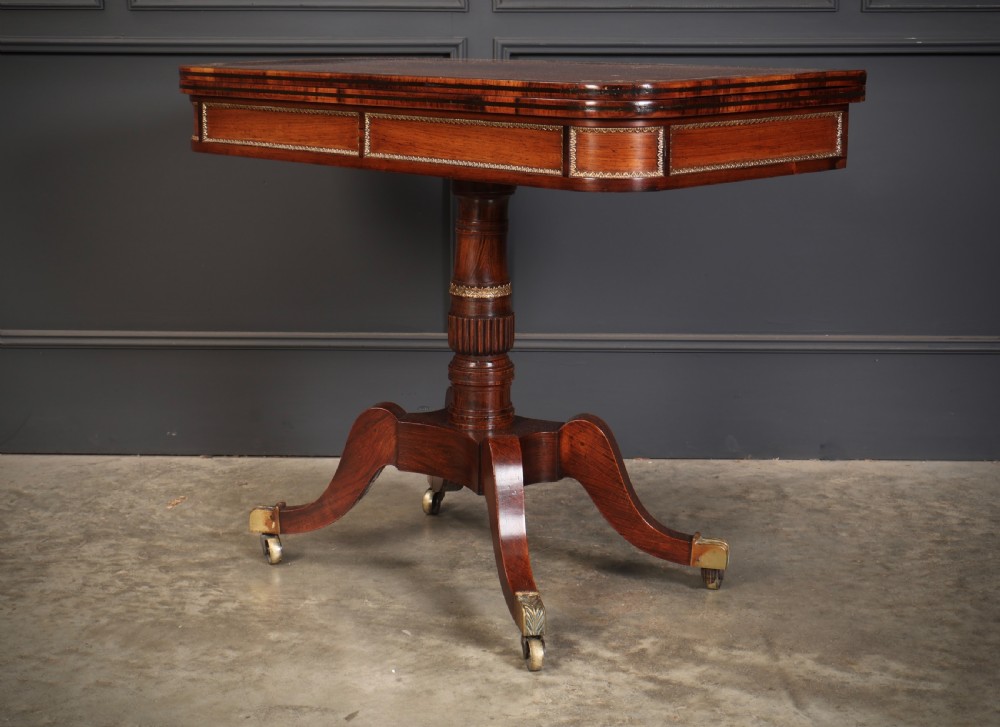 An antique Regency rosewood fold-over card table featuring brass inlay details, a turned pedestal stem, and four swept legs with brass castors. View XIV