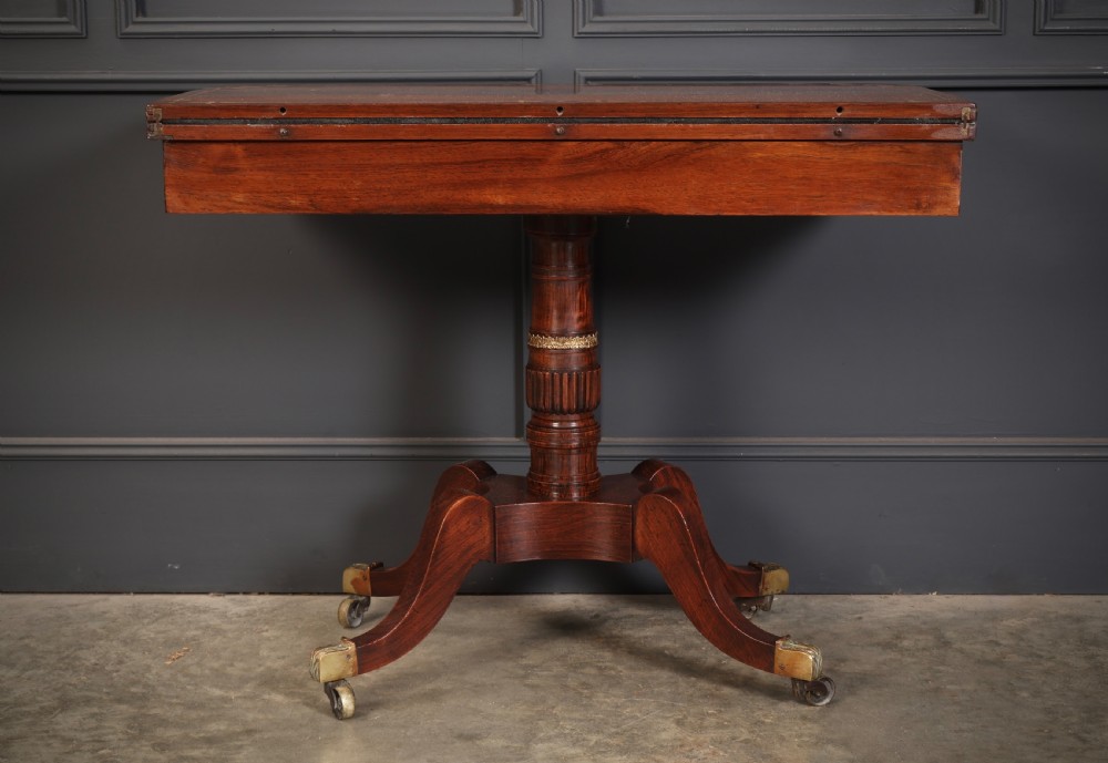 An antique Regency rosewood fold-over card table featuring brass inlay details, a turned pedestal stem, and four swept legs with brass castors. View XVI
