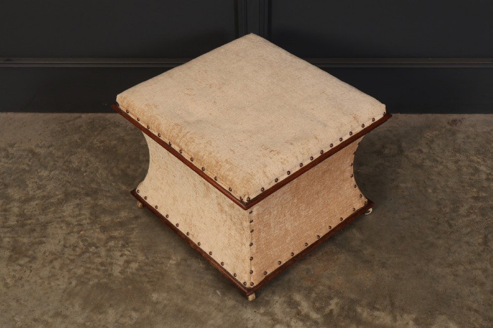 A square Regency box ottoman upholstered in textured beige fabric with dark mahogany trim, brass stud detailing, and small wheel castors. View II