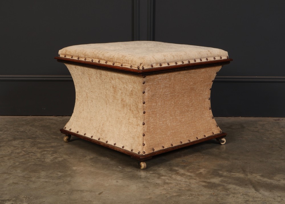 A square Regency box ottoman upholstered in textured beige fabric with dark mahogany trim, brass stud detailing, and small wheel castors. View III