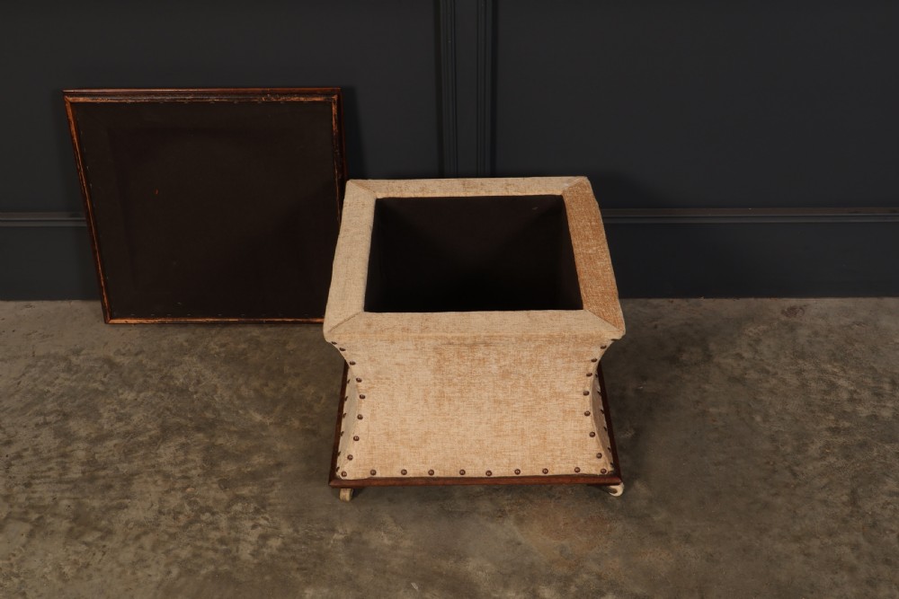 A square Regency box ottoman upholstered in textured beige fabric with dark mahogany trim, brass stud detailing, and small wheel castors. View VII