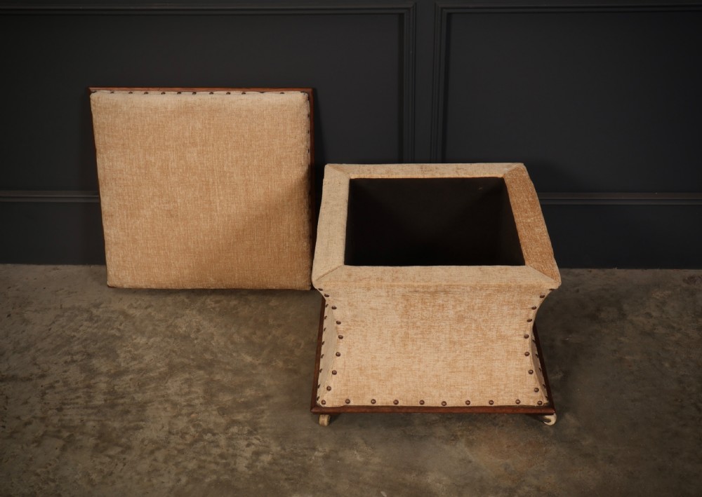 A square Regency box ottoman upholstered in textured beige fabric with dark mahogany trim, brass stud detailing, and small wheel castors. View VIII