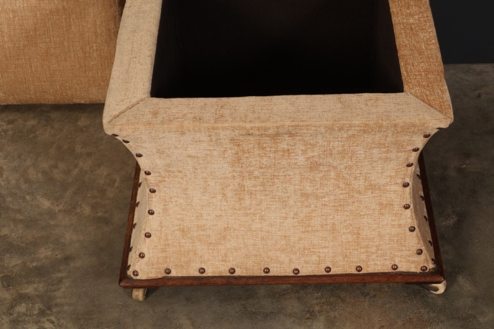 A square Regency box ottoman upholstered in textured beige fabric with dark mahogany trim, brass stud detailing, and small wheel castors. View IX