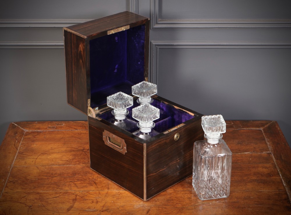 A Victorian coromandel wood decanter box lined with purple velvet, containing four square cut-glass decanters with faceted square stoppers.