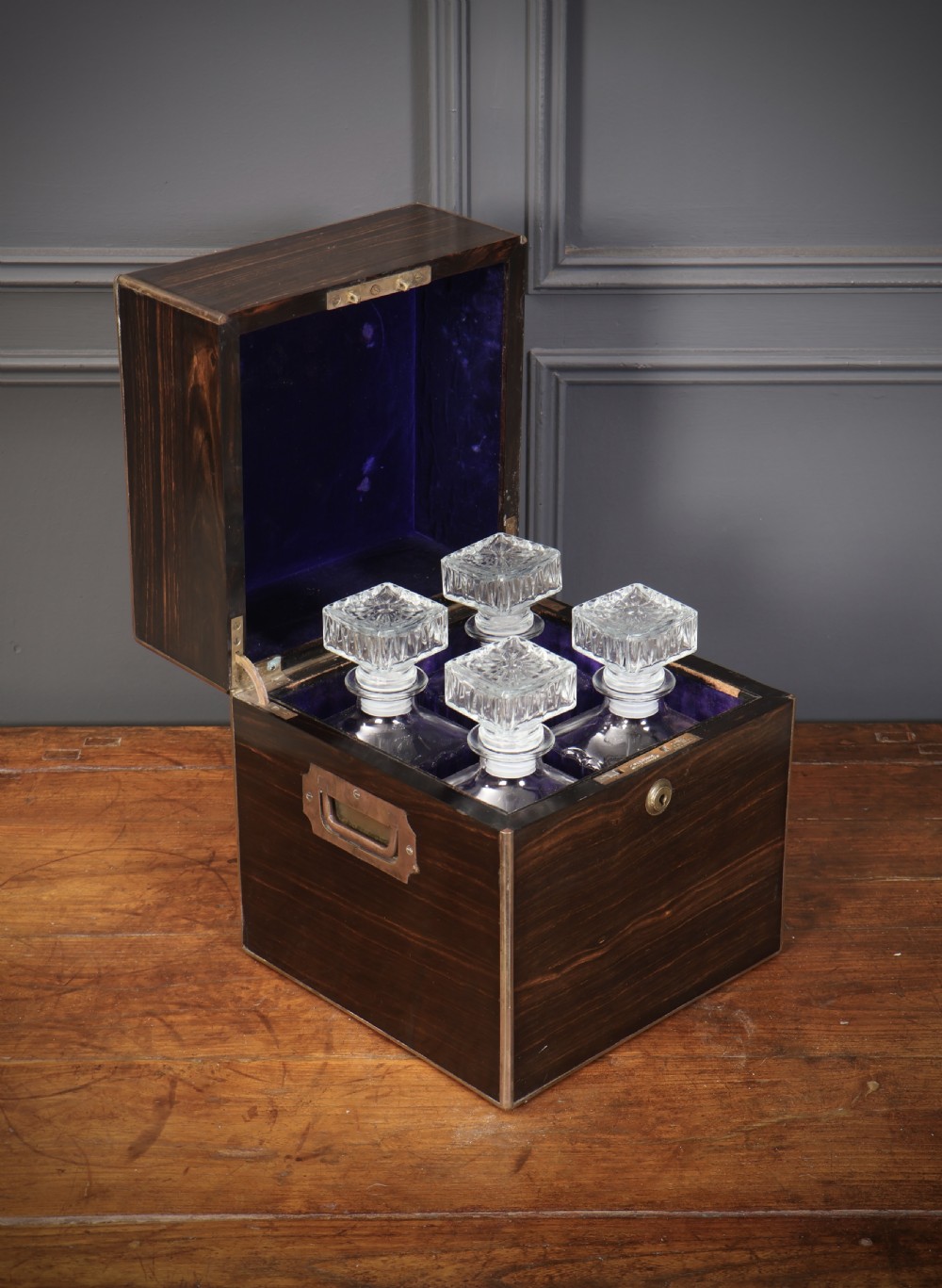 A Victorian coromandel wood decanter box lined with purple velvet, containing four square cut-glass decanters with faceted square stoppers. View VI