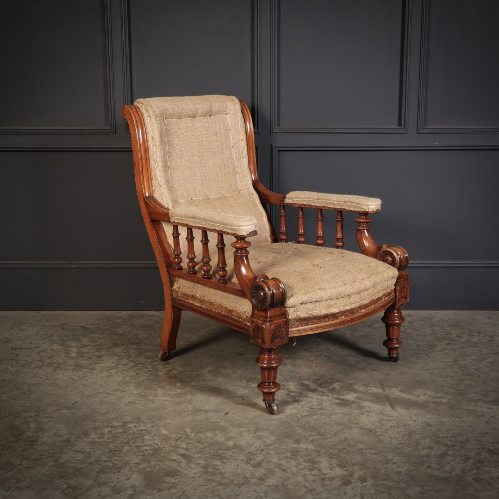 Victorian walnut library armchair with carved scroll arms, turned spindle supports, turned front legs on castors, and hessian lining.