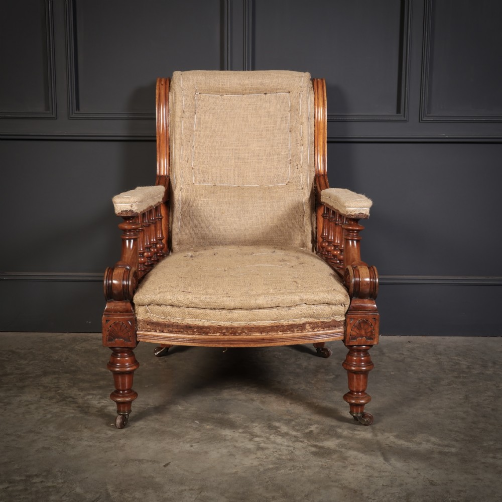 Victorian walnut library armchair with carved scroll arms, turned spindle supports, turned front legs on castors, and hessian lining. View II