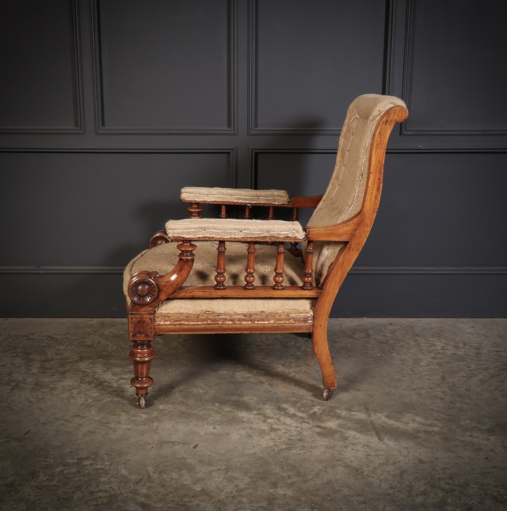 Victorian walnut library armchair with carved scroll arms, turned spindle supports, turned front legs on castors, and hessian lining. View III