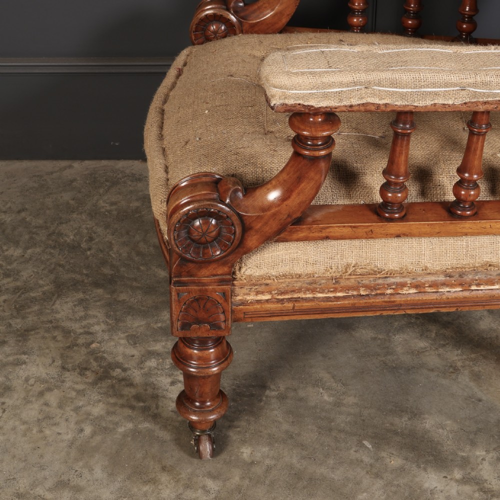 Victorian walnut library armchair with carved scroll arms, turned spindle supports, turned front legs on castors, and hessian lining. View V