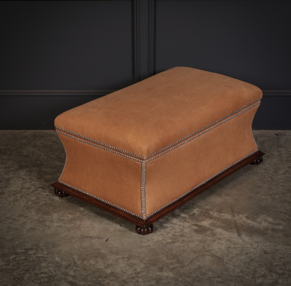 A rectangular tan leather upholstered box ottoman featuring brass stud trim and concave sides on a dark rosewood plinth base with turned feet.