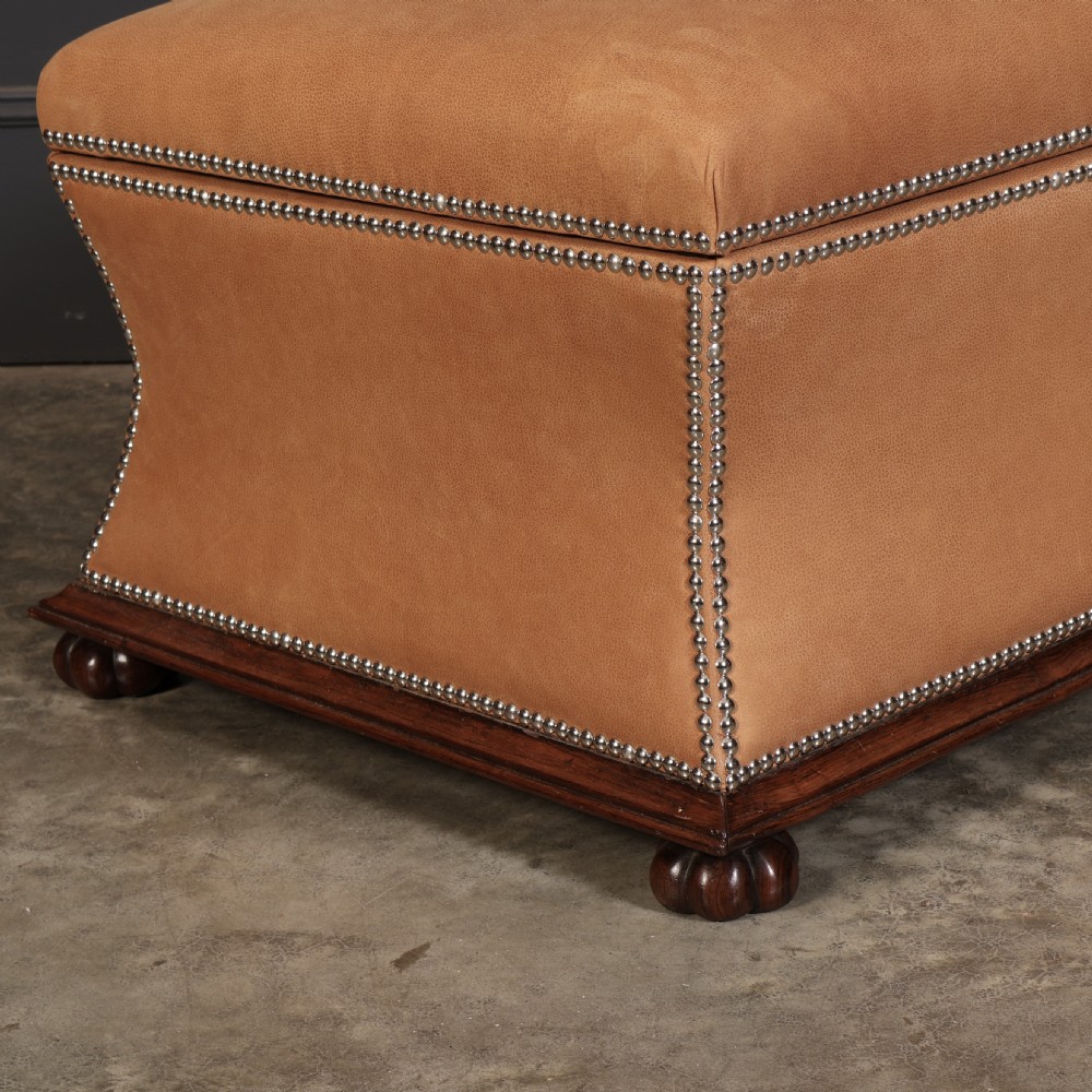 A rectangular tan leather upholstered box ottoman featuring brass stud trim and concave sides on a dark rosewood plinth base with turned feet. View II