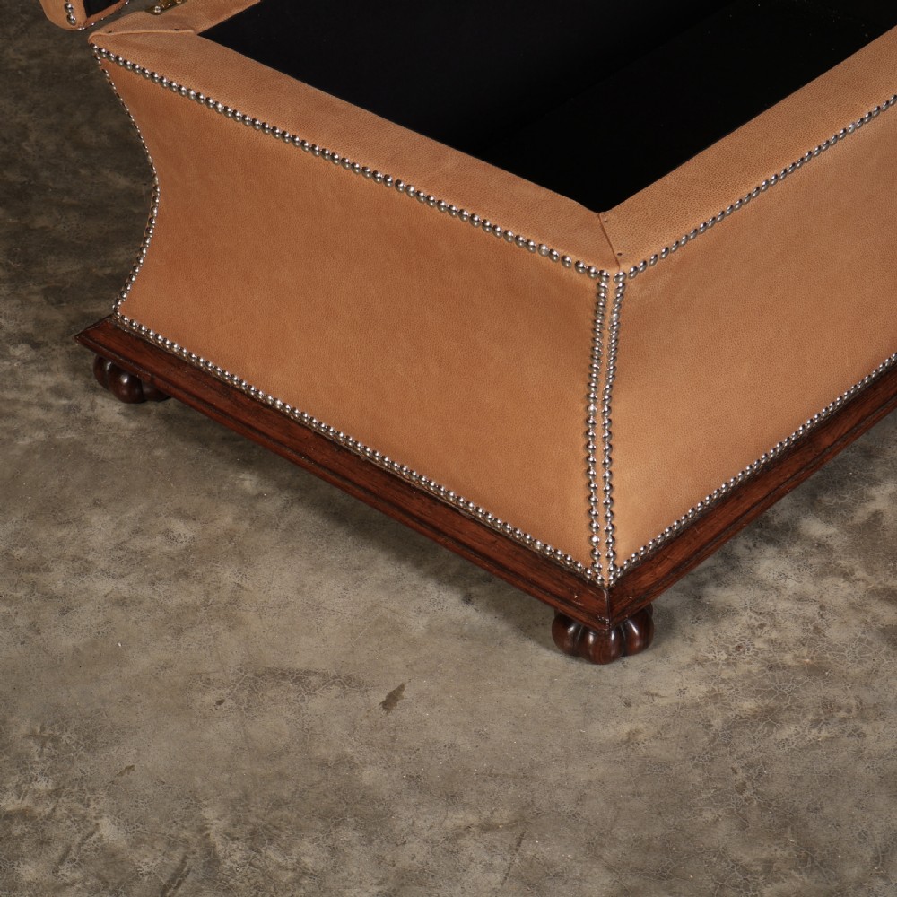 A rectangular tan leather upholstered box ottoman featuring brass stud trim and concave sides on a dark rosewood plinth base with turned feet. View III