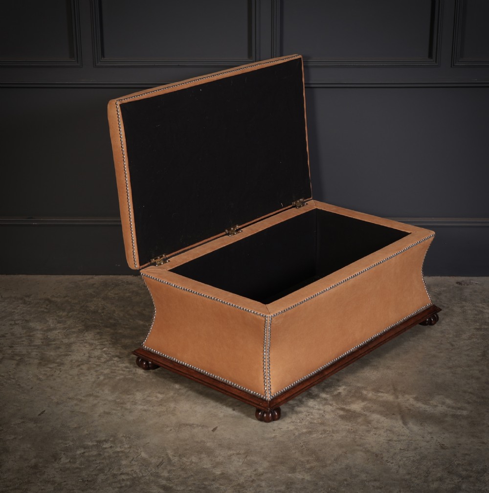 A rectangular tan leather upholstered box ottoman featuring brass stud trim and concave sides on a dark rosewood plinth base with turned feet. View V