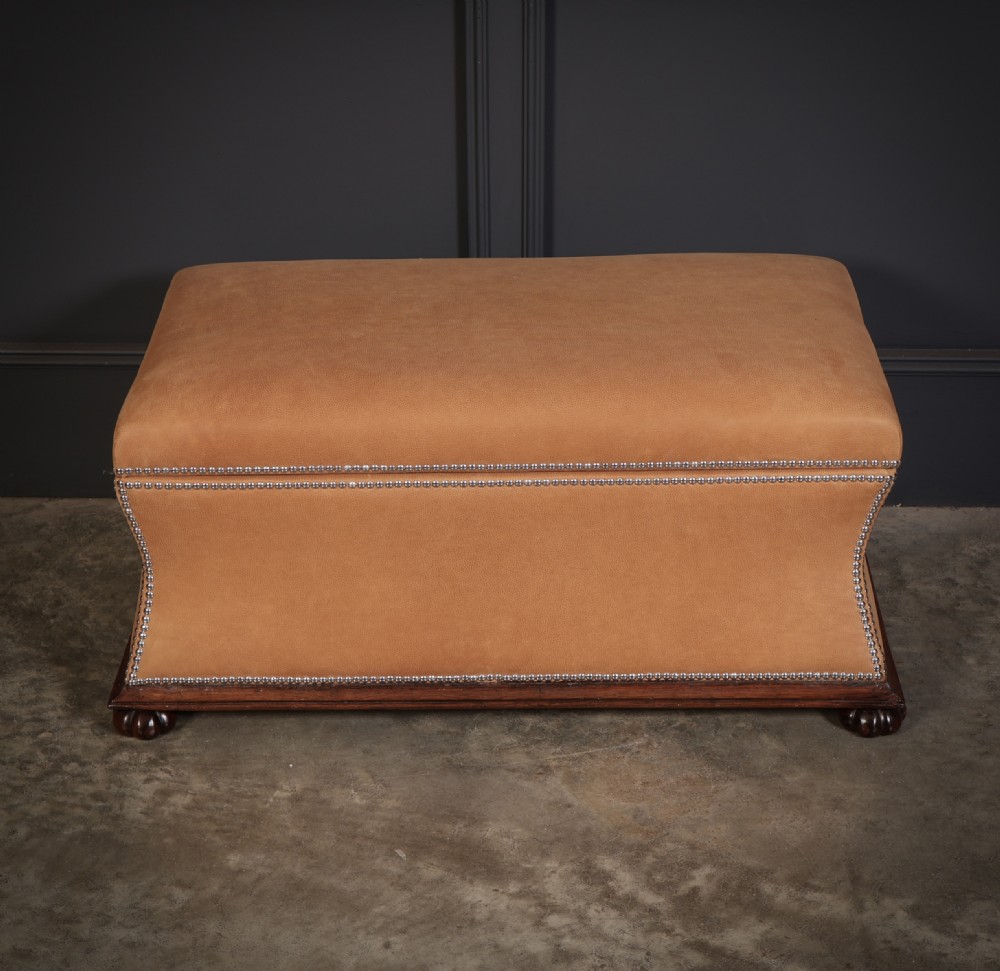A rectangular tan leather upholstered box ottoman featuring brass stud trim and concave sides on a dark rosewood plinth base with turned feet. View VI