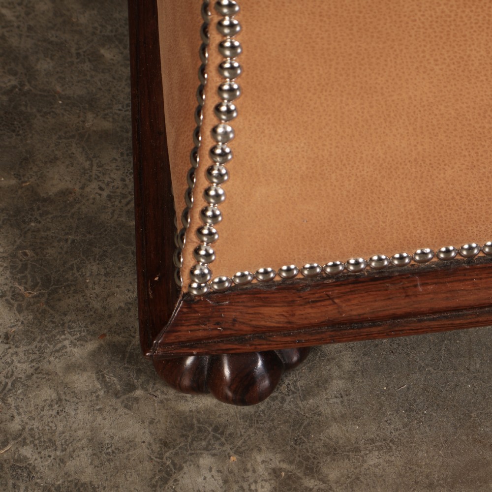 A rectangular tan leather upholstered box ottoman featuring brass stud trim and concave sides on a dark rosewood plinth base with turned feet. View IX