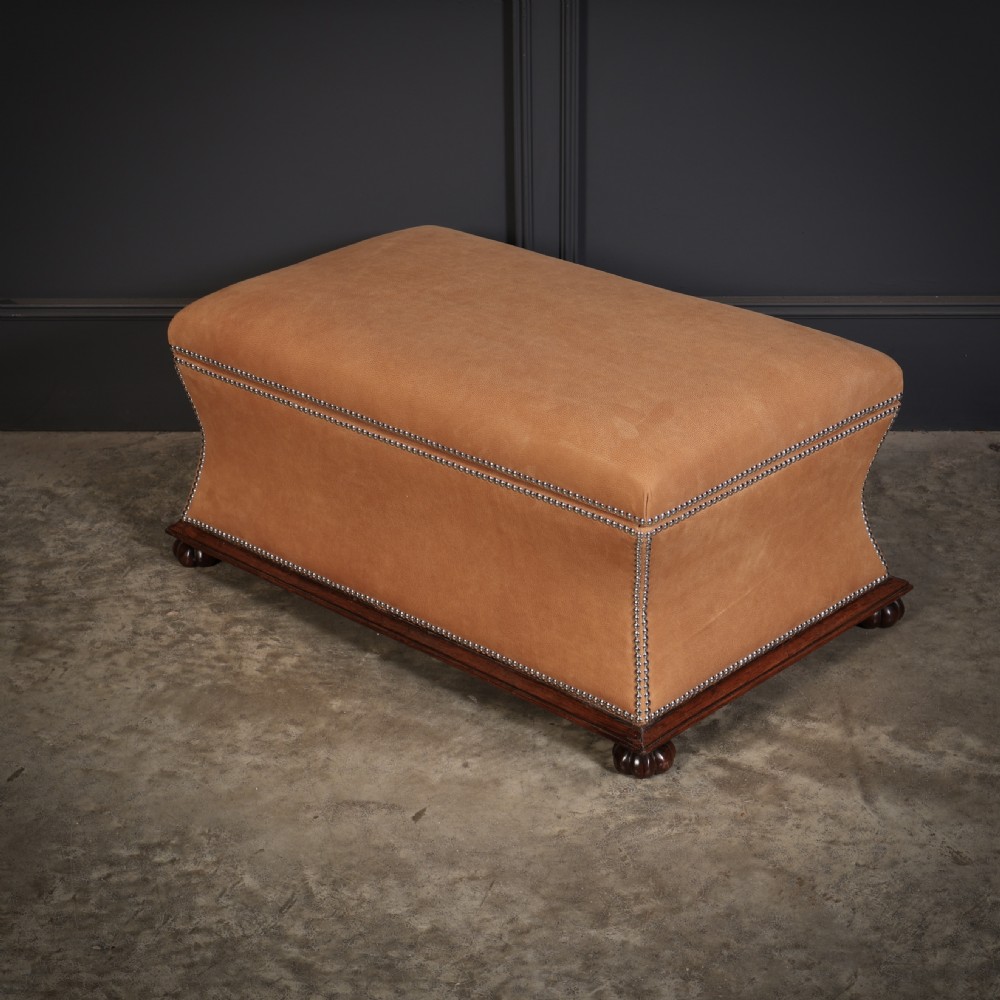 A rectangular tan leather upholstered box ottoman featuring brass stud trim and concave sides on a dark rosewood plinth base with turned feet. View X
